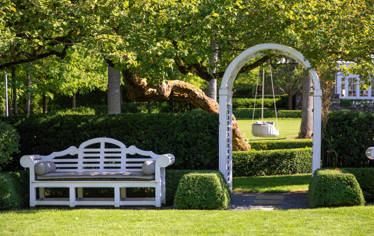 Formal residential garden entrance with a Lutyen's bench, pergola and linear evergreen hedges.