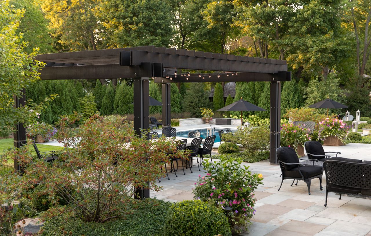 Modern wood and steel pergola set within a natural stone terrace overlooking the swimming pool.