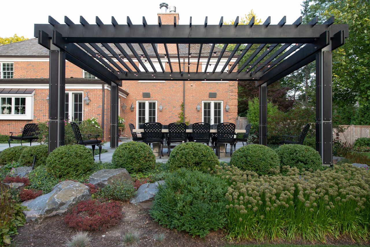 Modern wood and steel pergola with dining table set within a garden.