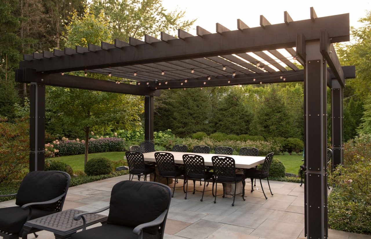Modern wood and steel pergola with dining table set overlooking the backyard garden.