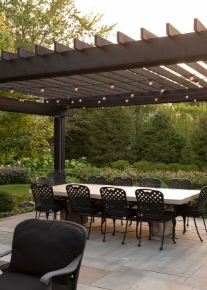 Modern wood and steel pergola with dining table set overlooking the backyard garden.