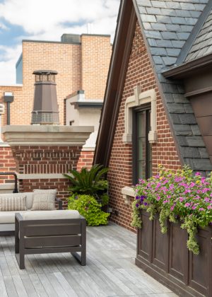 Chicago rooftop garden with flowers, palm trees, and beige outdoor sofa.