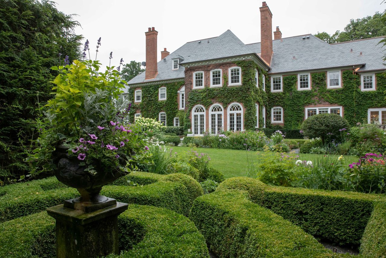 Boxwood parterre garden with flowers in dark, traditional urn, on a large, ivy covered, suburban estate.