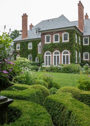 Boxwood parterre garden with flowers in dark, traditional urn, on a large, ivy covered, suburban estate.