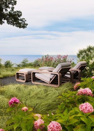 Tranquil lounge area under large maple, surrounded by colorful hydrangeas, with a view of the lake.