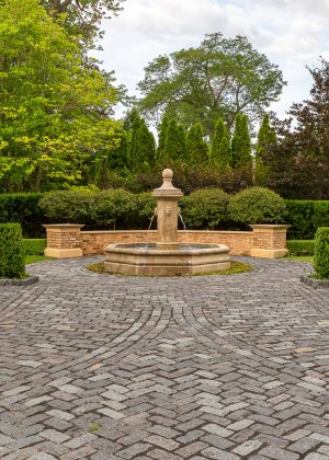 Cobblestone brick driveway with a large fountain and well trimmed boxwood hedges.