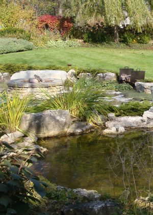 Pond with fire pit in background, mowed lawn surround by flower beds