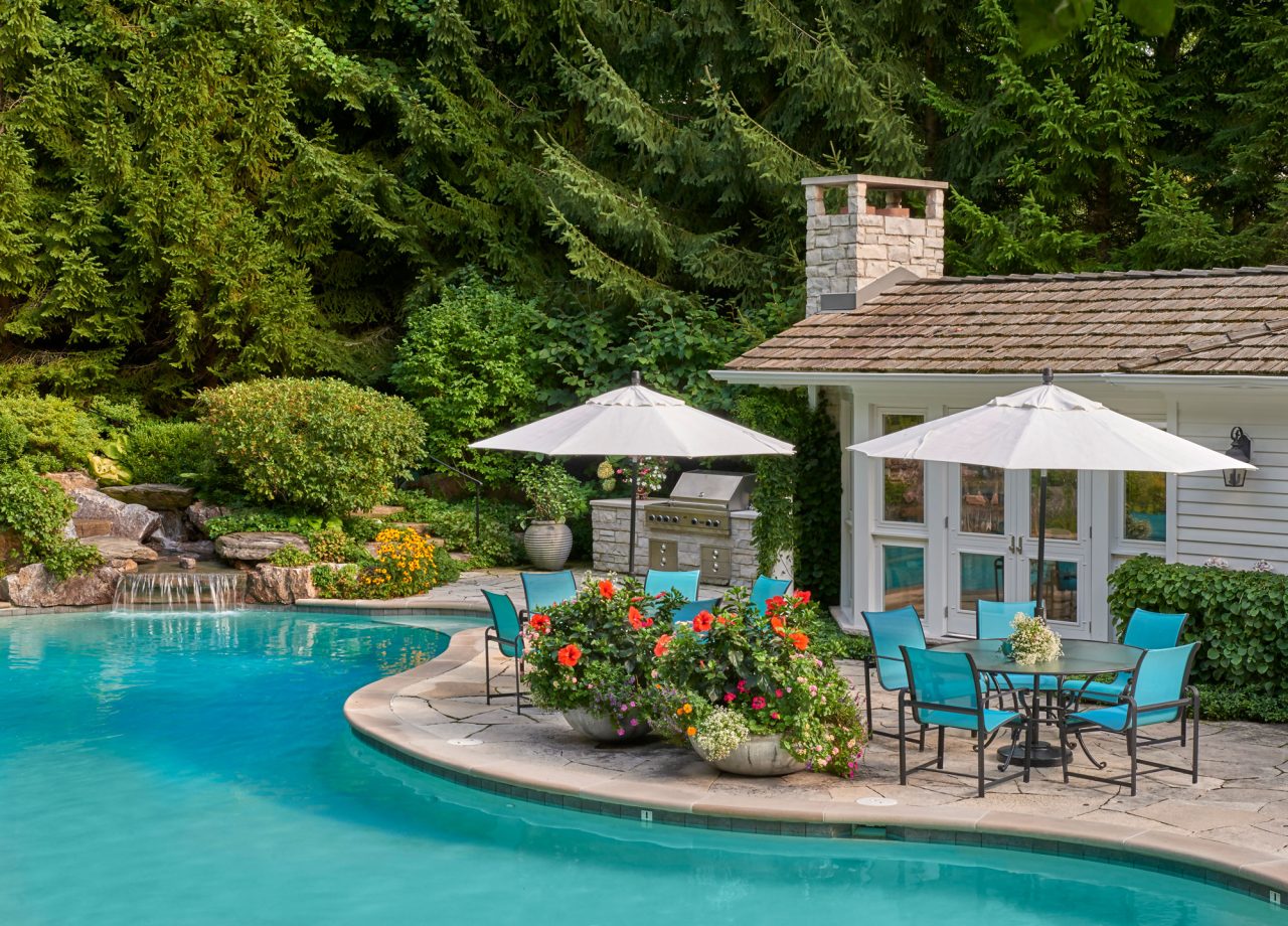 Waterfall cascading into pool with outdoor seating surrounded with bright annuals