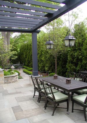 Bluestone deck, cobblestone flower beds, black metal pergola with hanging lanterns, and arborvitae hedge