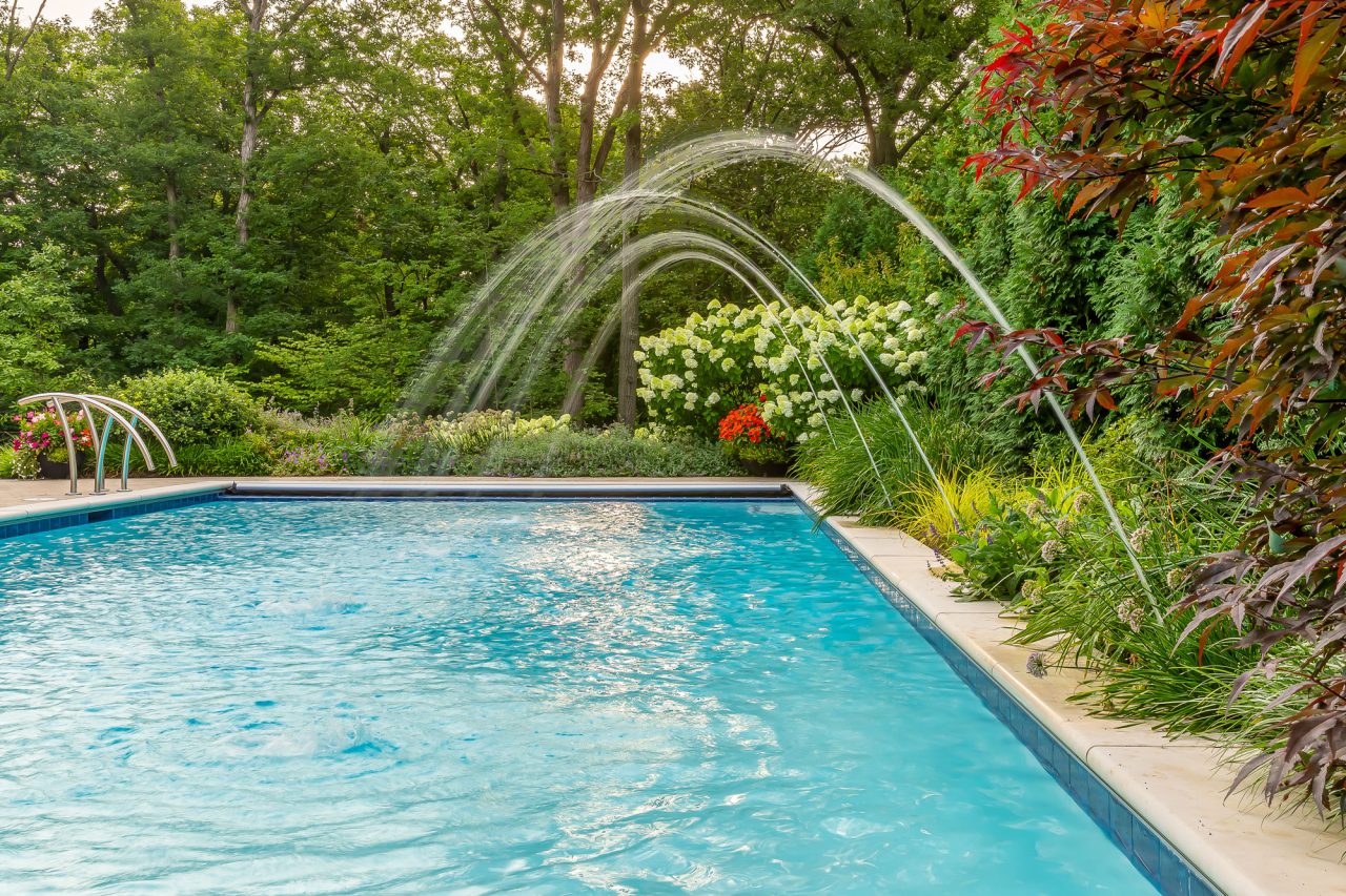 Water jets playfully splash around the pool. Surrounded by perennial garden