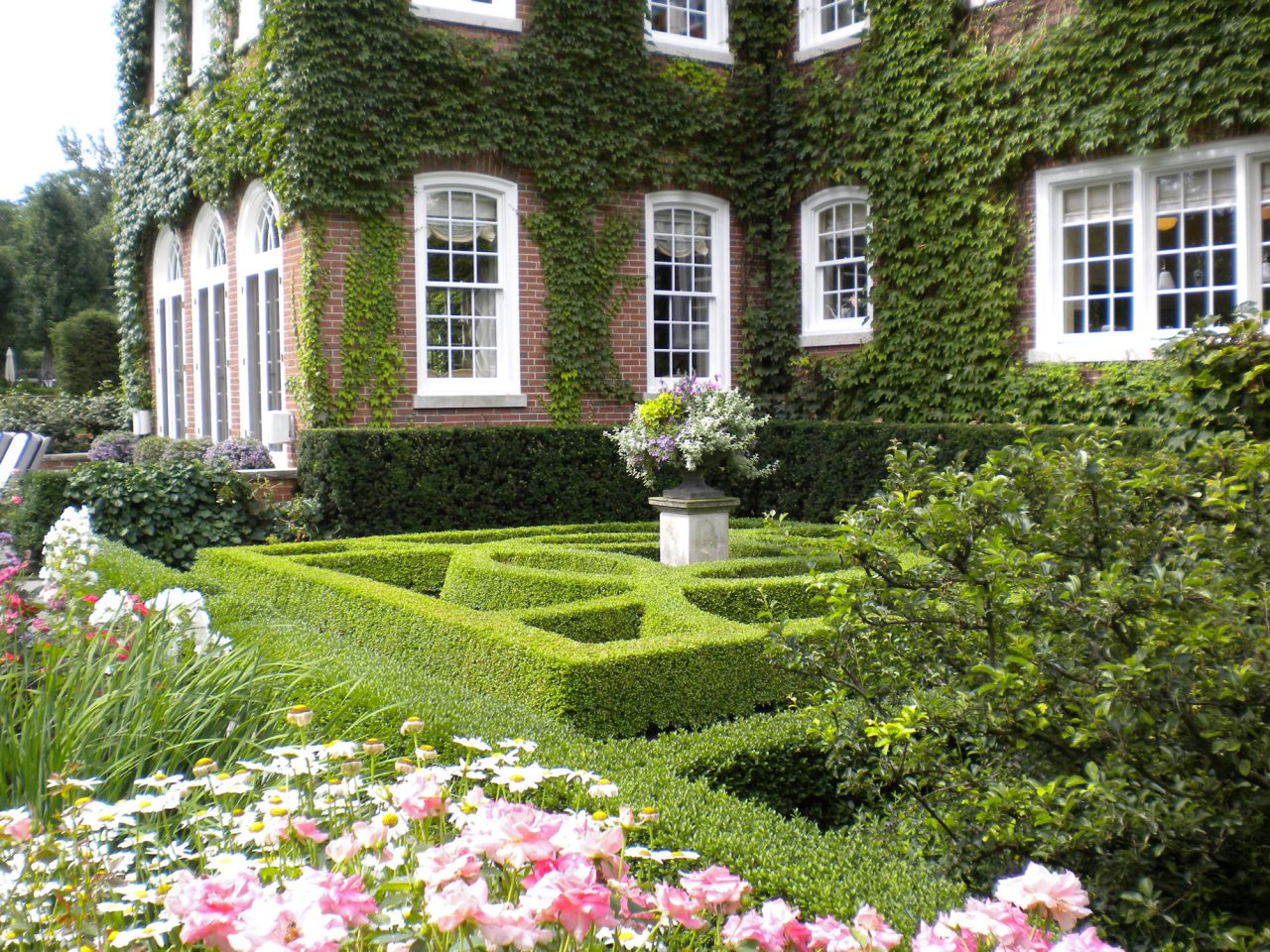Beautiful boxwood parterre in perennial garden with annual container on pedestal