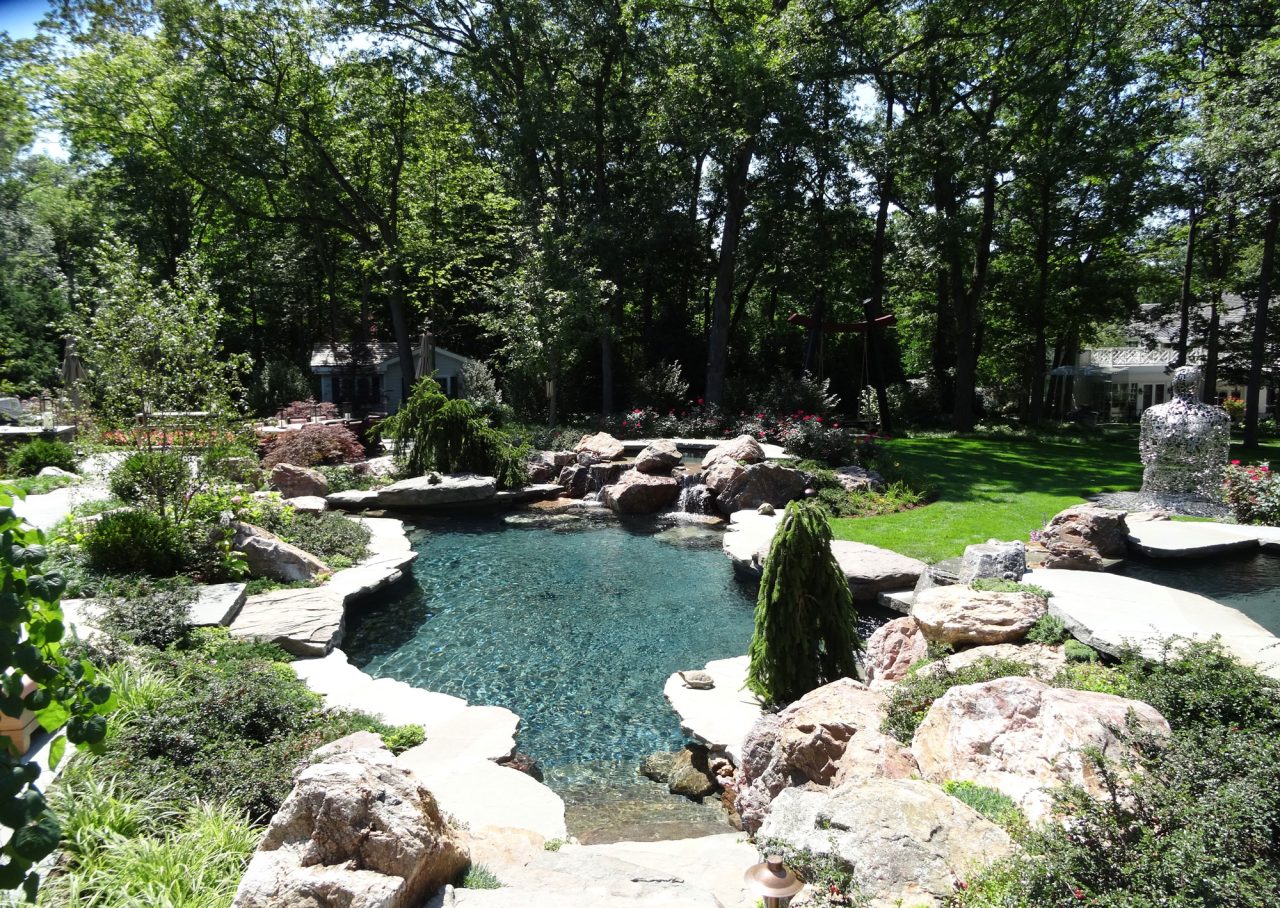 Naturalized pool with waterfall and boulder edges accented by sculpture and natural landscape