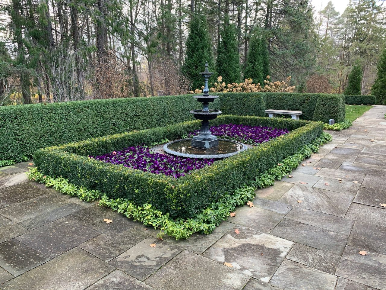 Three-tiered fountain surrounded by boxed hedges, annuals, and groundcover