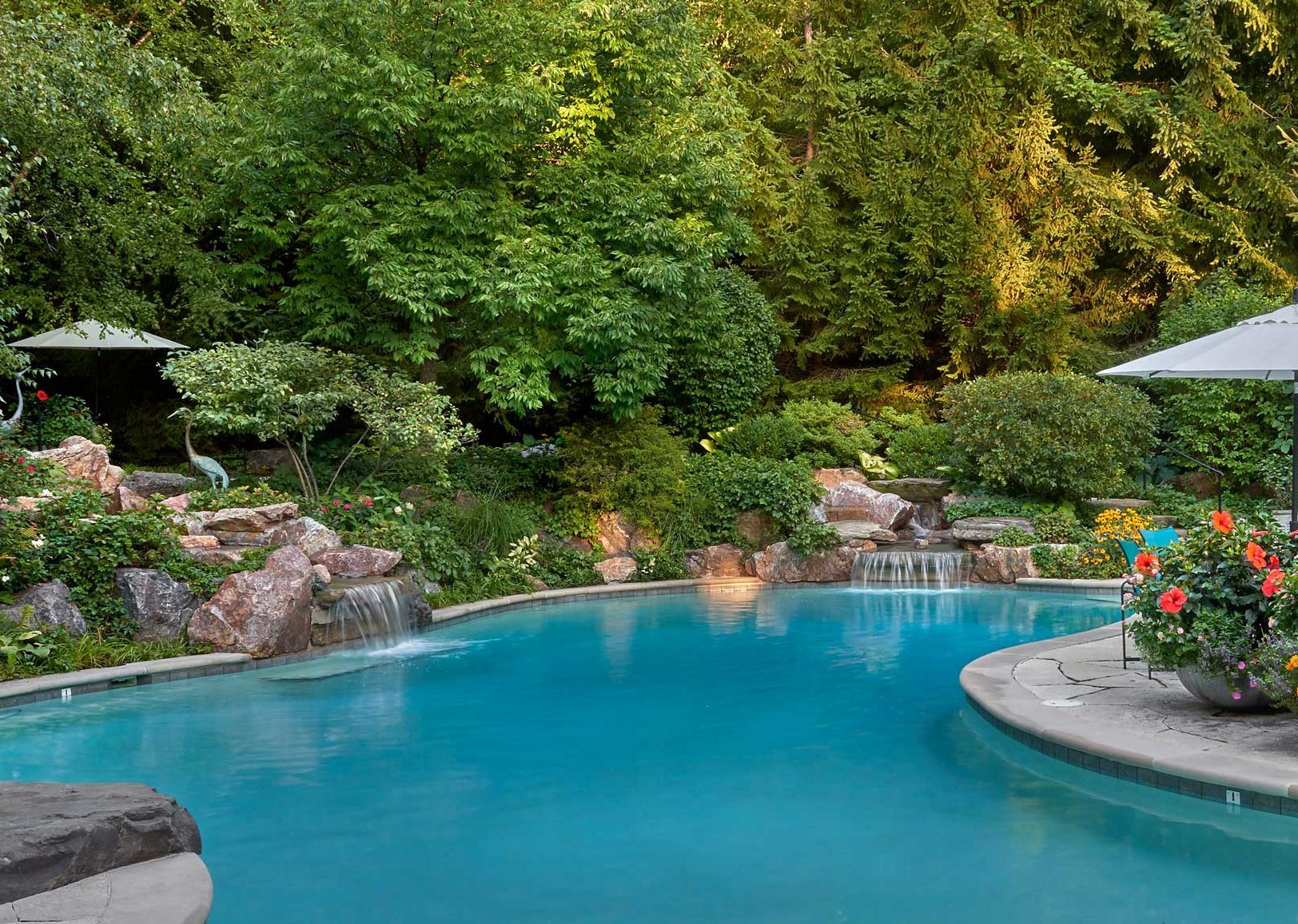 Huge swimming pool with waterfalls, stone deck and large potted plant arrangements by Midwest landscape architect.